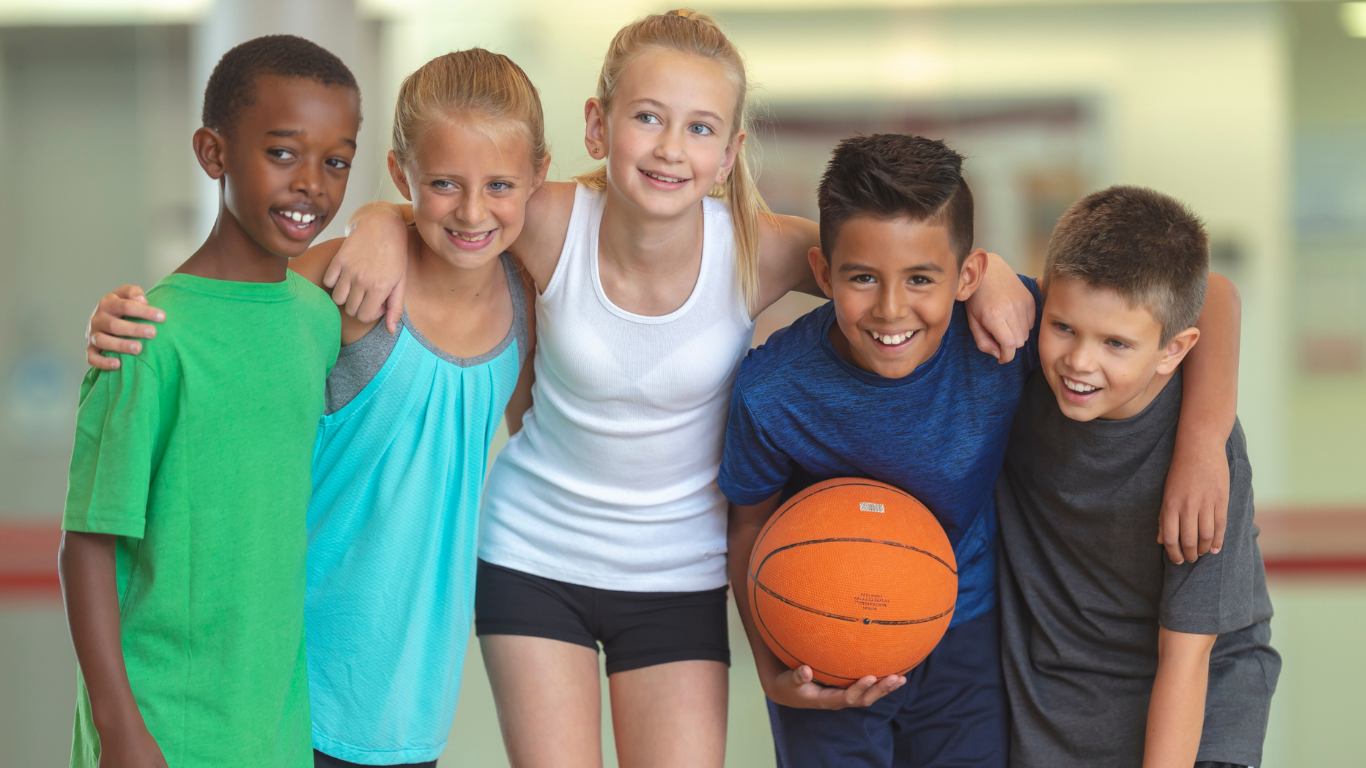 Five children smiling in a gym with one holding a basketball